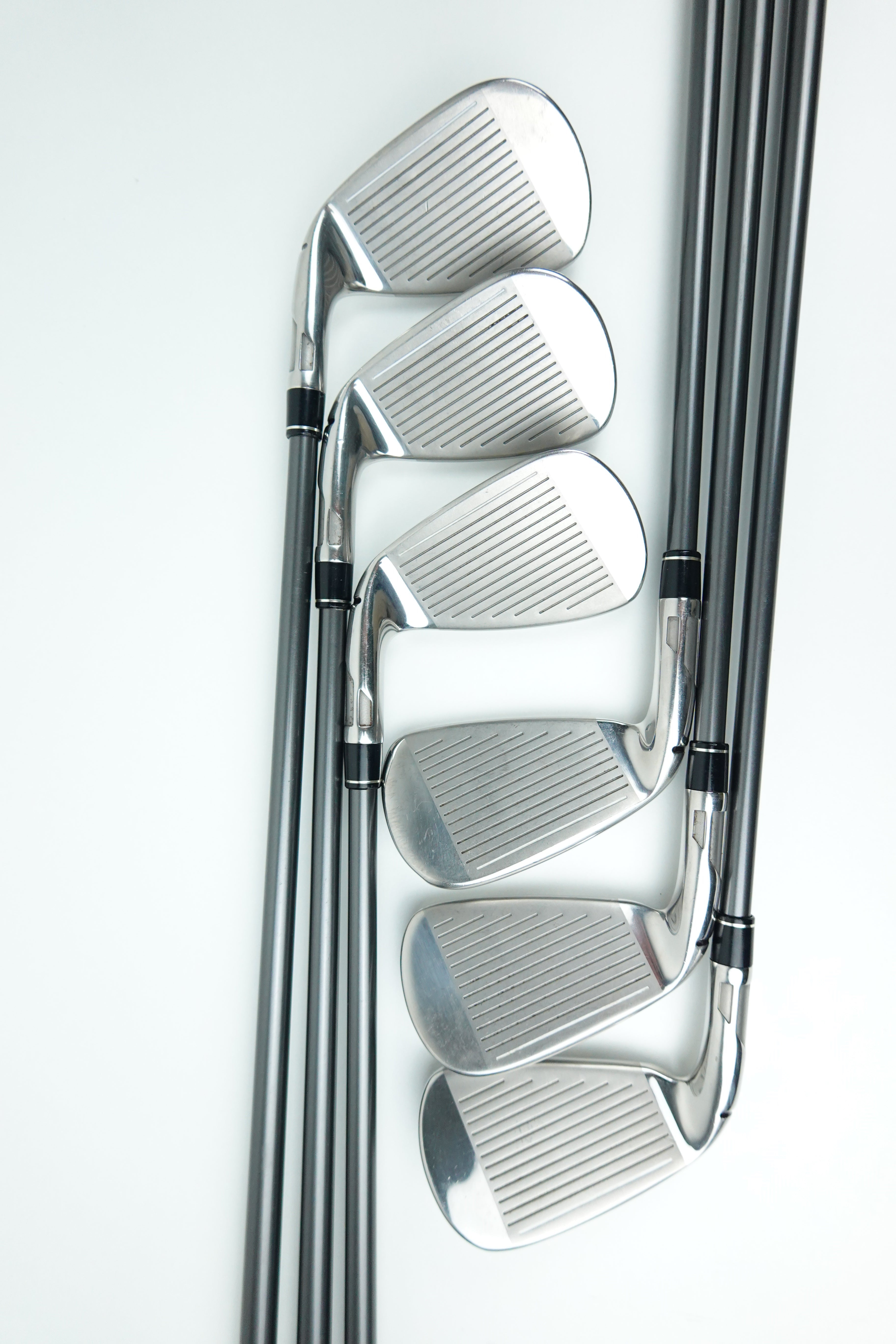 A set of six golf iron clubs arranged in a fan pattern on a clean white background, showing their polished silver metal heads and dark shafts.