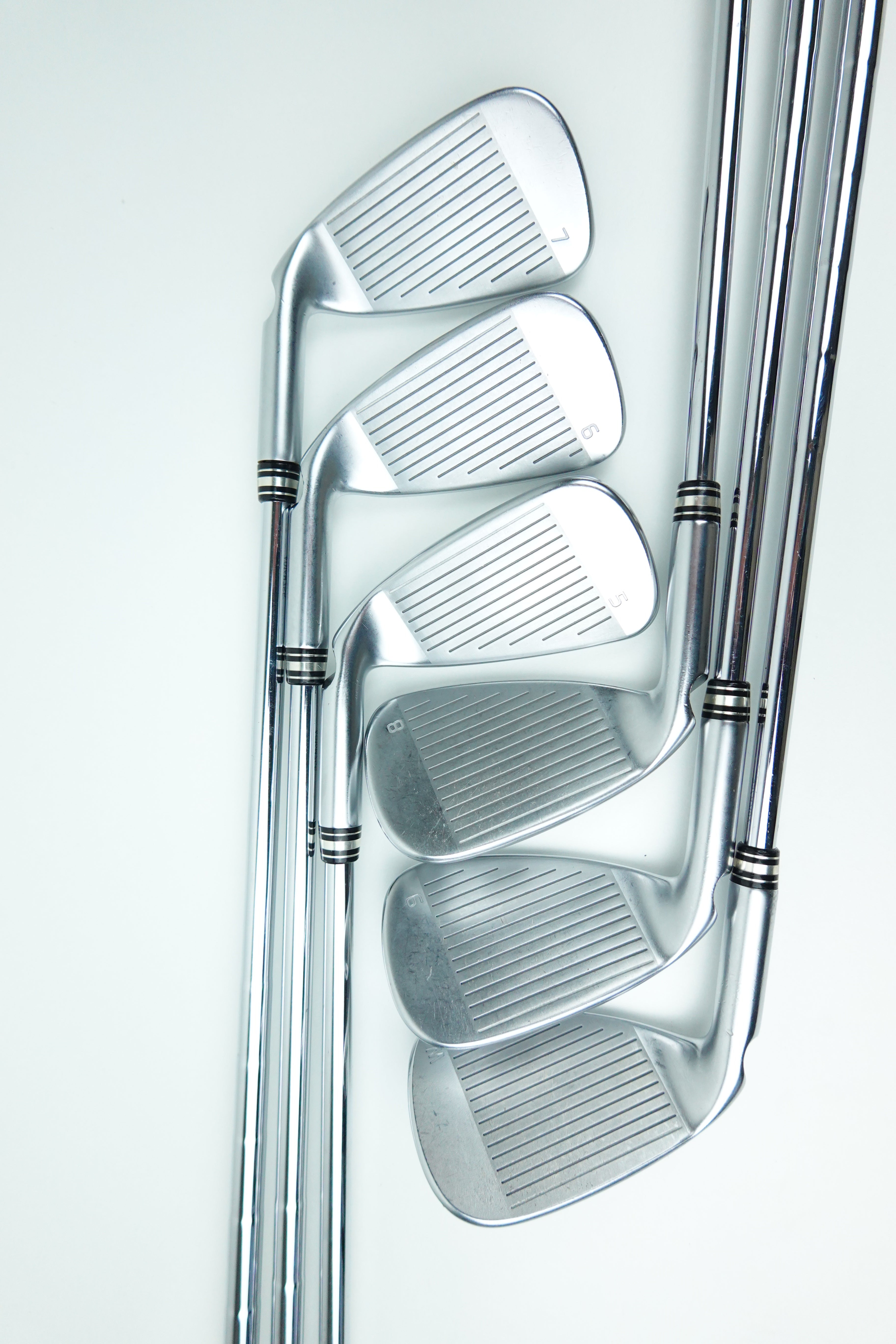 A set of five polished silver golf irons arranged diagonally on a clean white background.