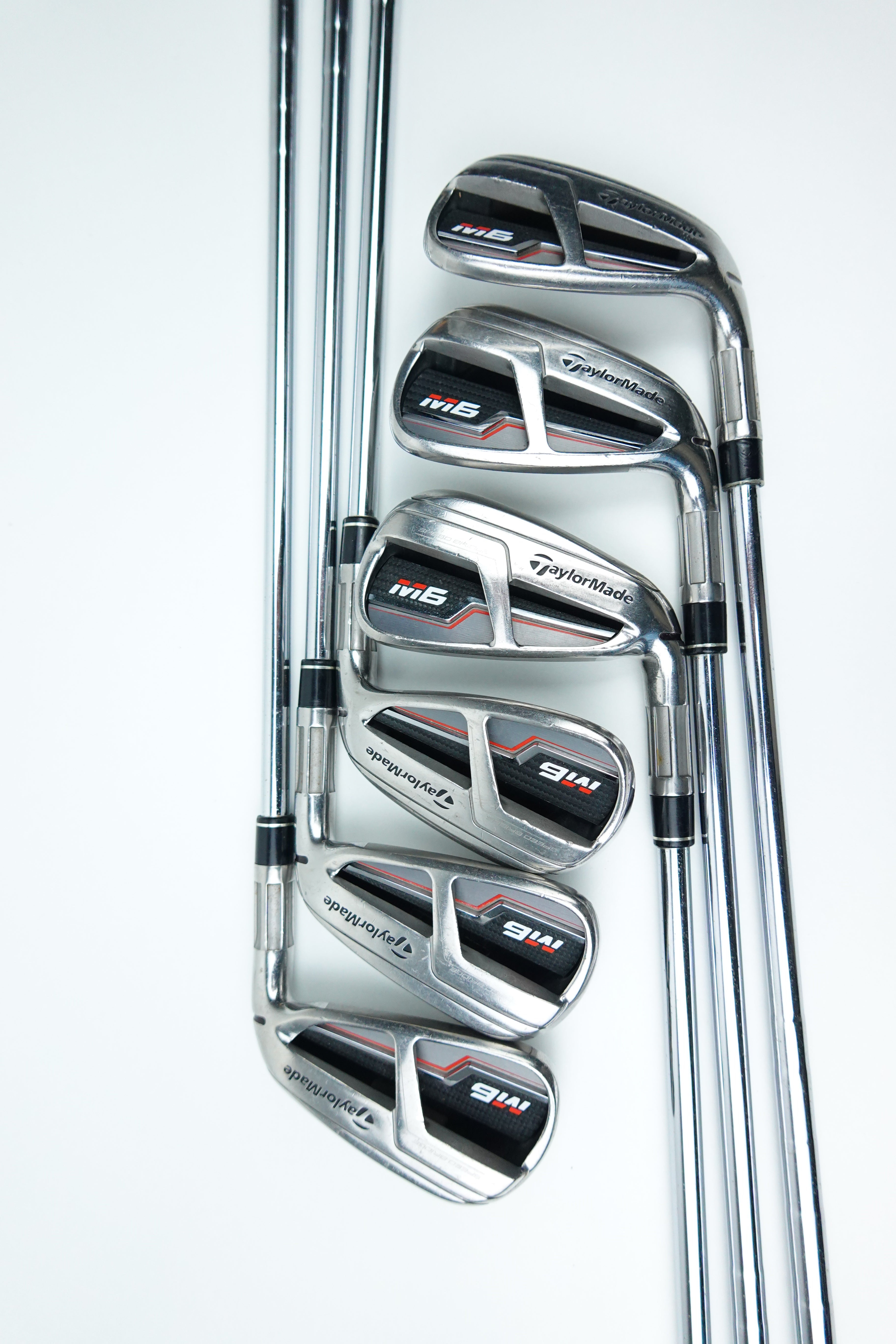 A set of six TaylorMade M6 golf iron clubs arranged diagonally on a clean white background, showing their polished metal heads and chrome shafts.