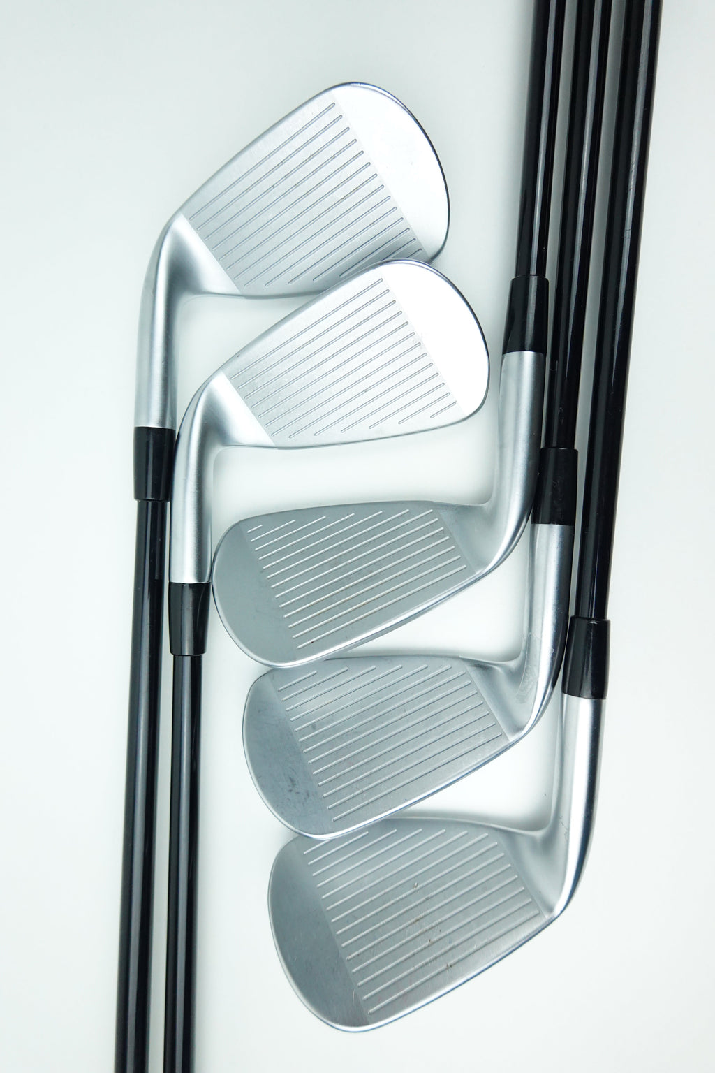 Four golf iron clubs with silver metal heads and black shafts, arranged diagonally on a clean white background.