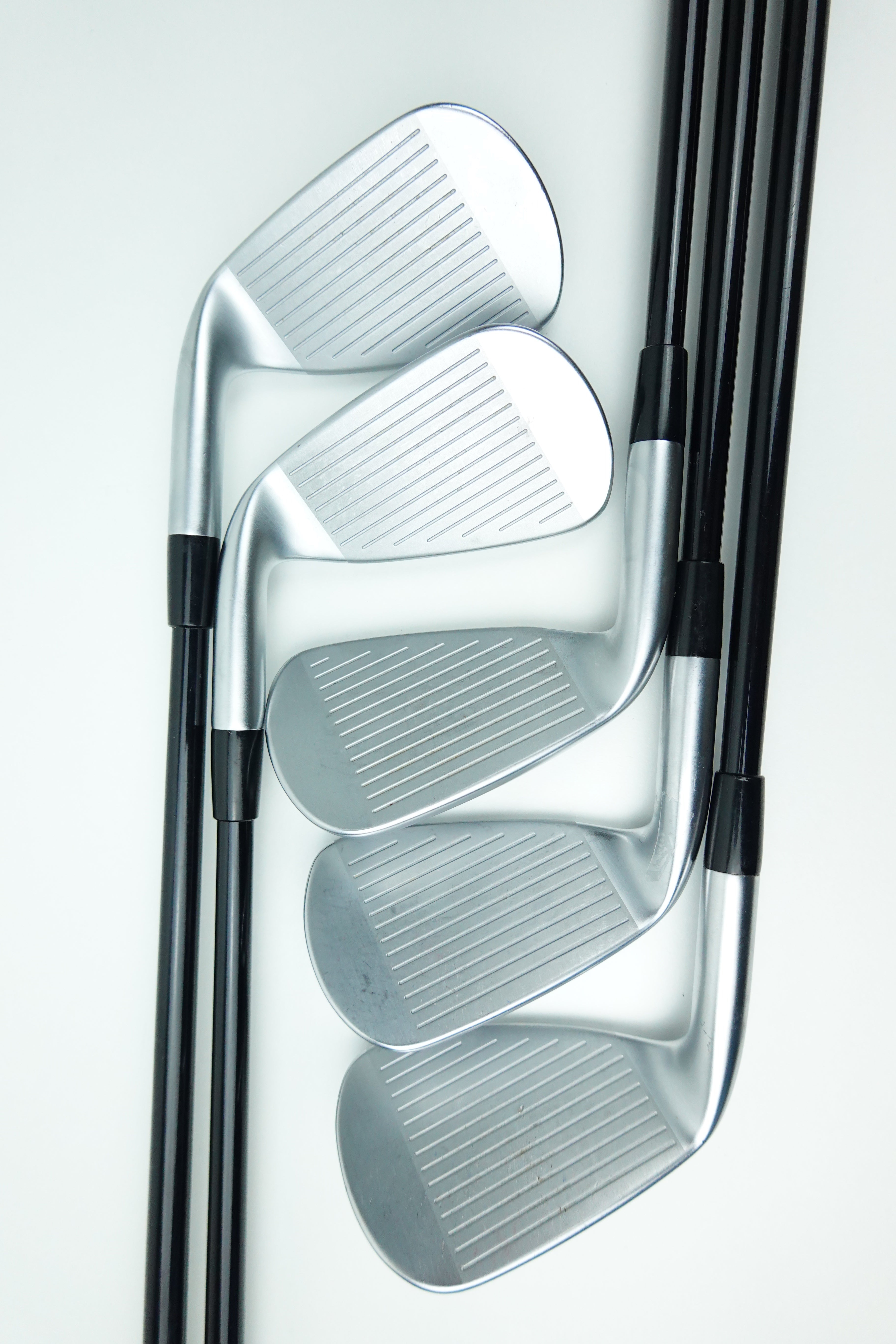 Four golf iron clubs with silver metal heads and black shafts, arranged diagonally on a clean white background.