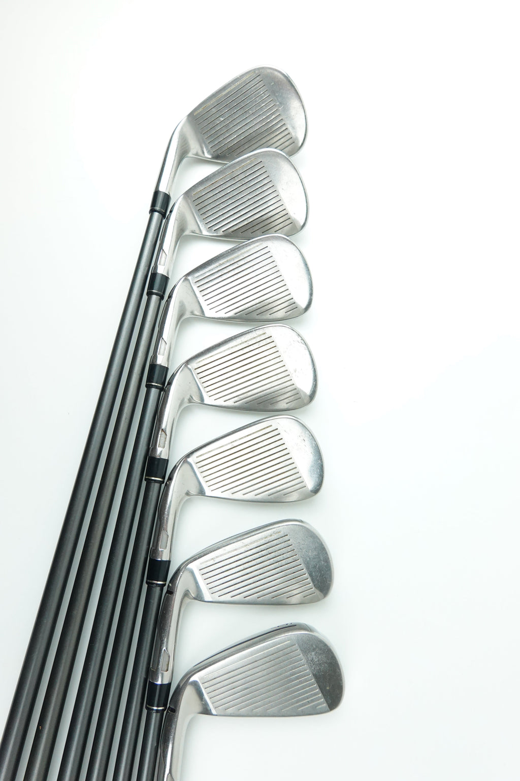 A set of eight golf iron clubs with silver metal heads and black shafts, arranged in a neat diagonal row on a clean white background.