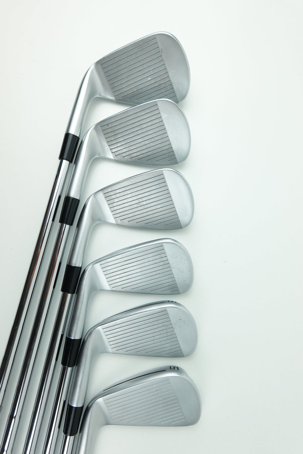 A set of seven silver metal golf iron clubs arranged in a fan pattern against a plain white background.